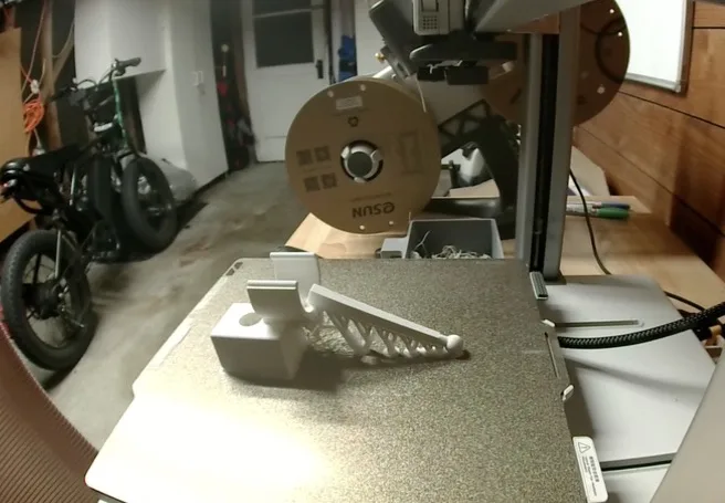 The finished reprint on the printer bed: a small clamp on the left and the mic cradle with its long boom held up by branching tree supports on the right.