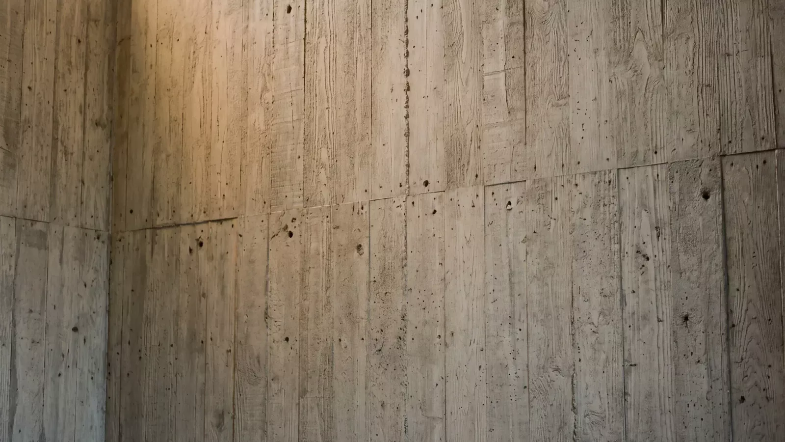 A wall of board-marked concrete in raking light, every plank's grain recorded in the surface.