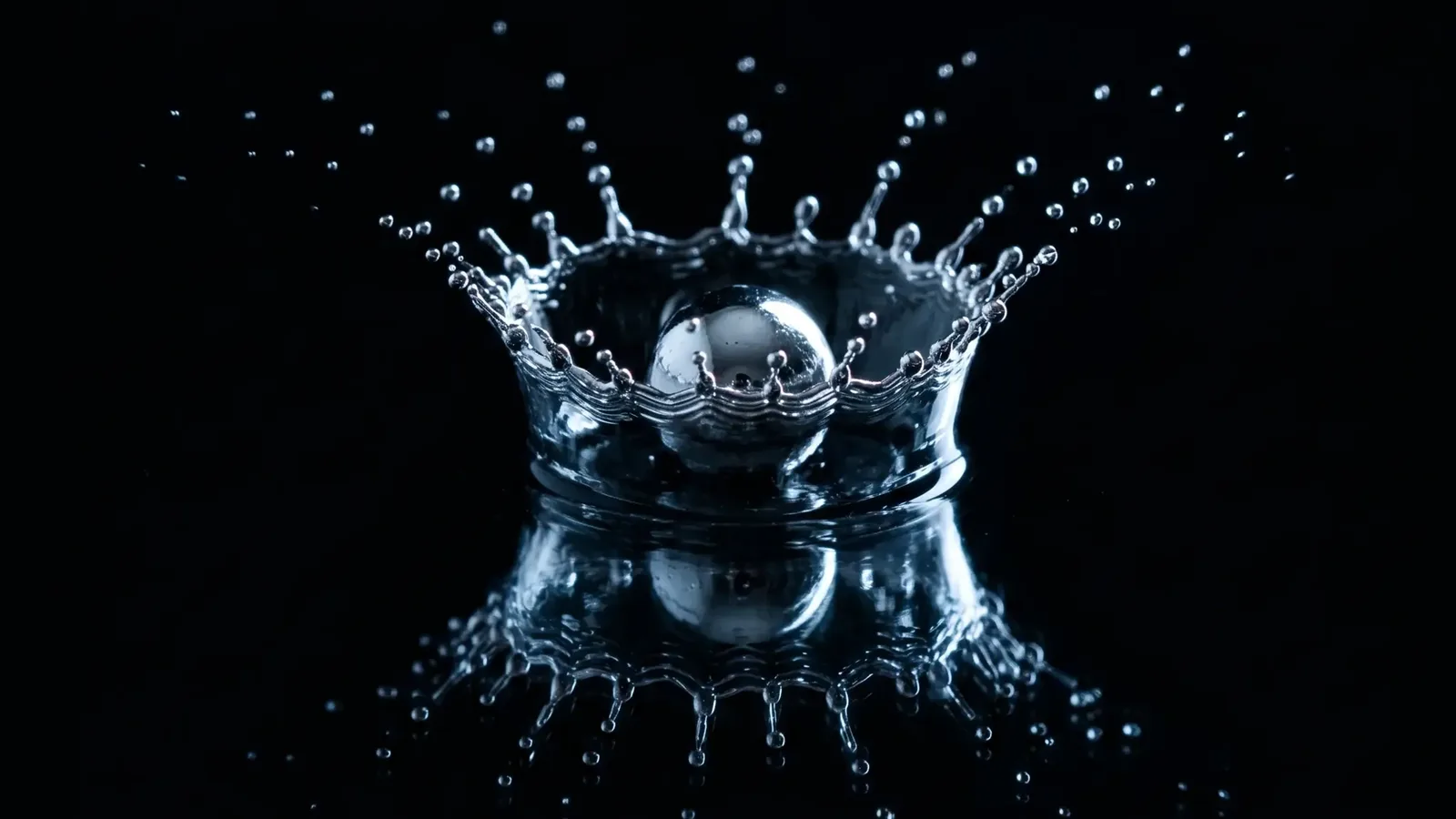 A chrome ball landing in water, throwing up a crown of droplets and reflected in the dark surface below.