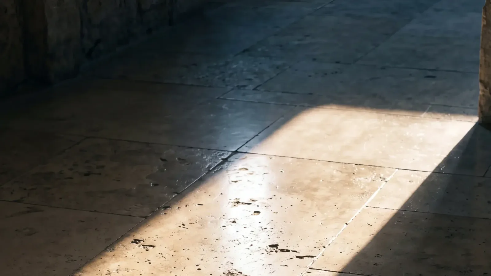 A shaft of sunlight falls through a single opening across a dark travertine floor, the one bright path in an otherwise shadowed room.